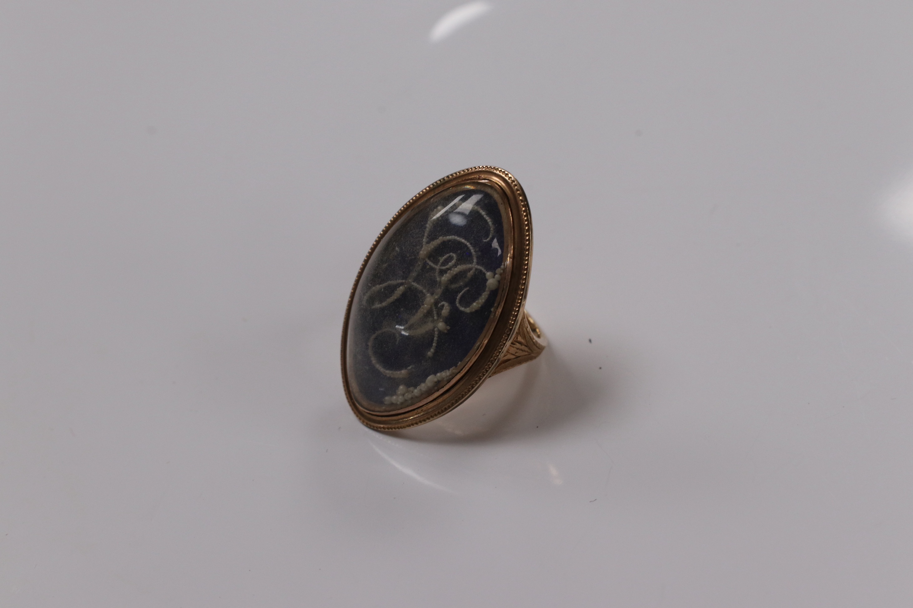 A George III yellow metal, enamel and simulated seed pearl set initialled oval mourning ring, with engraved inscription, 'Isaac Sparks ob. 17th Jan, 1788 ae. 60' size G/H, gross weight 7.6 grams. Condition - poor